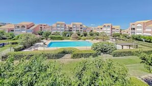 Et hotel med en swimmingpool omgivet af grønt og en klar blå himmel.