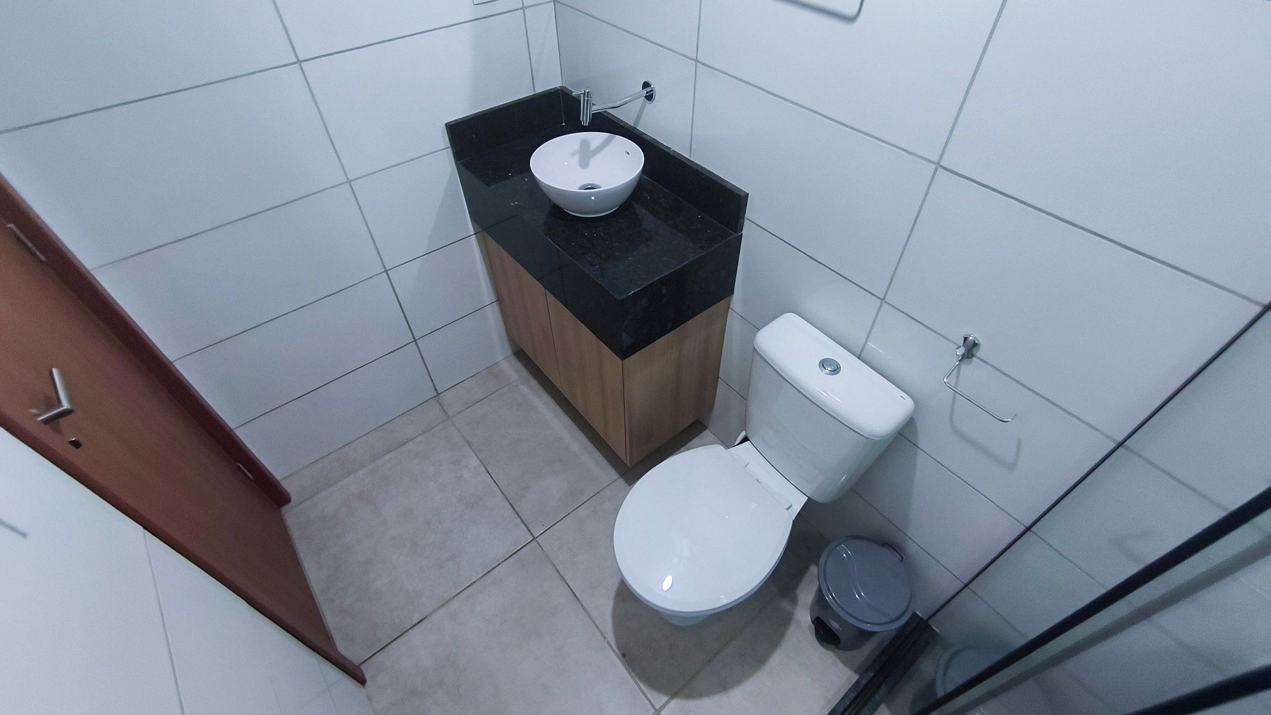 A small bathroom with a white toilet, a sink, and a trash bin.