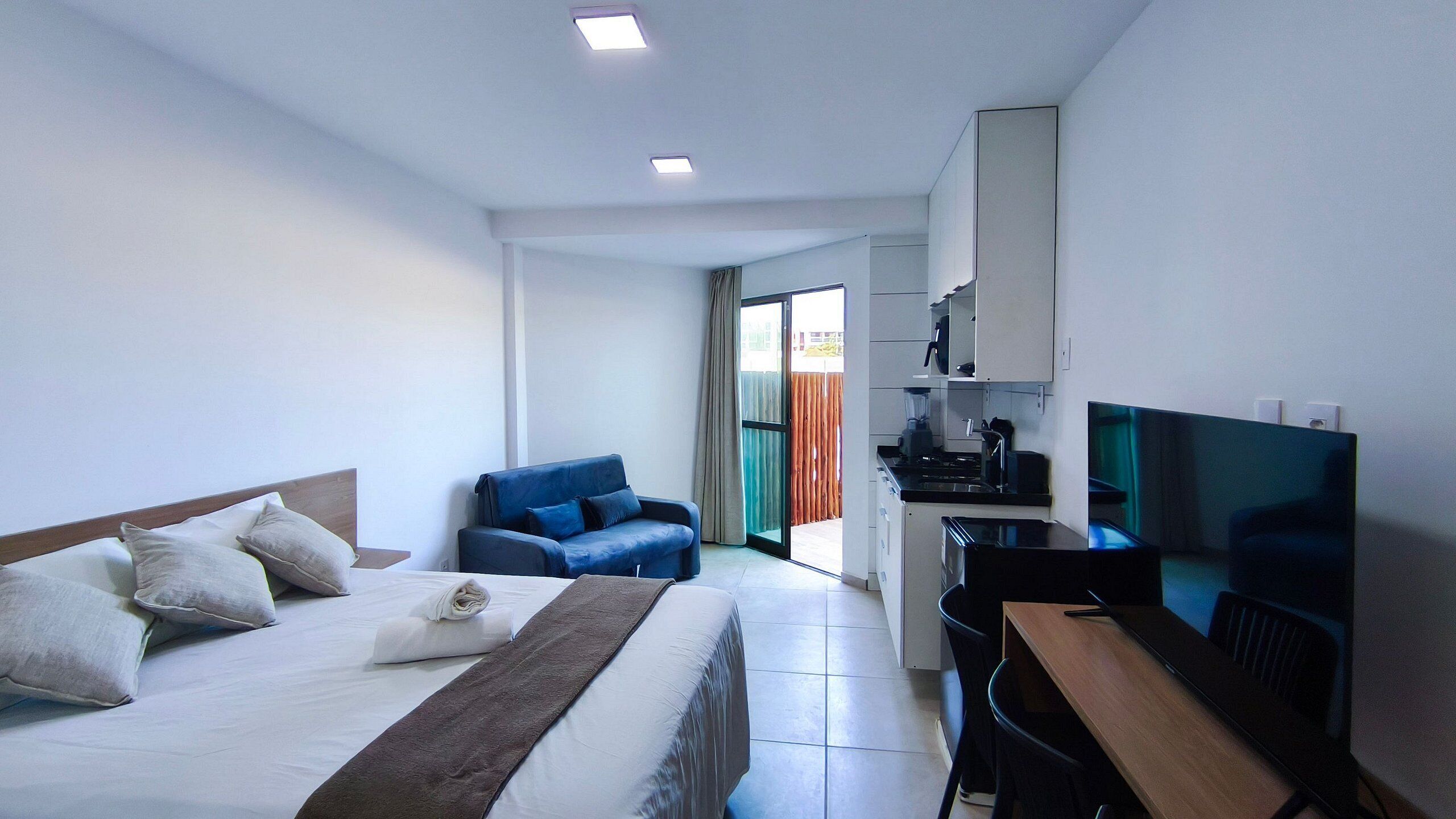Ein Hotelzimmer mit Bett, Schreibtisch, Stuhl, Fernseher und einer Küchenzeile.