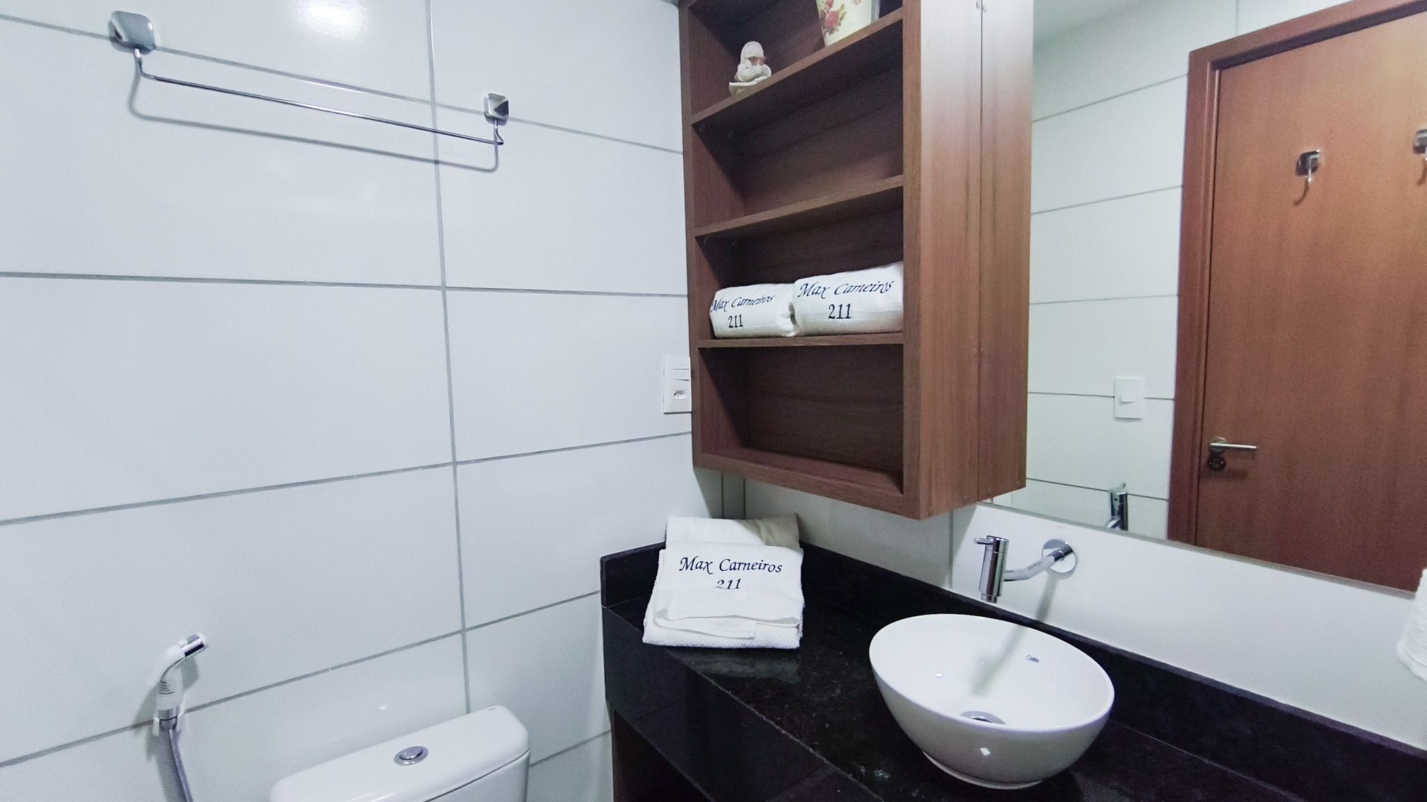 Une salle de bain comprenant des toilettes, un lavabo avec un miroir, un porte-serviettes et une étagère en bois avec des serviettes.