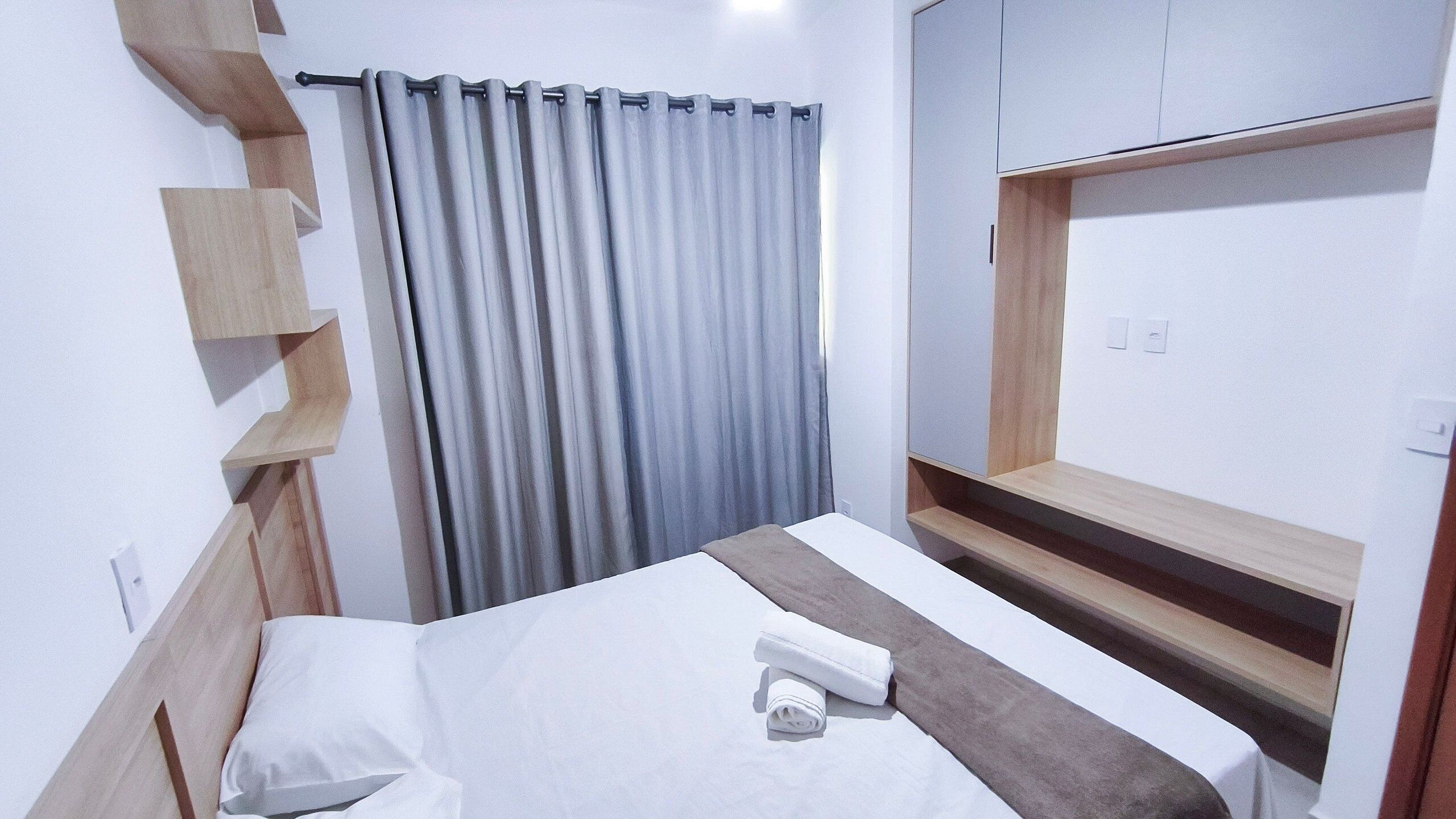 Ein Hotelzimmer mit Bett, einer Holzhängeschrank, einem grauen Vorhang und einem Einbauschrank.