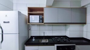 Cocina compacta con refrigerador, microondas, estufa y un estante de madera sobre el microondas.