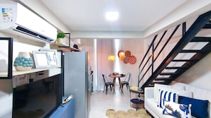 A compact living space with a dining area, a sofa, a staircase, and a kitchen area.
