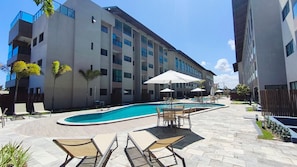 A modern building with a swimming pool, outdoor seating, and a fenced patio area. - Max Carneiros Suítes  (Tamandaré)