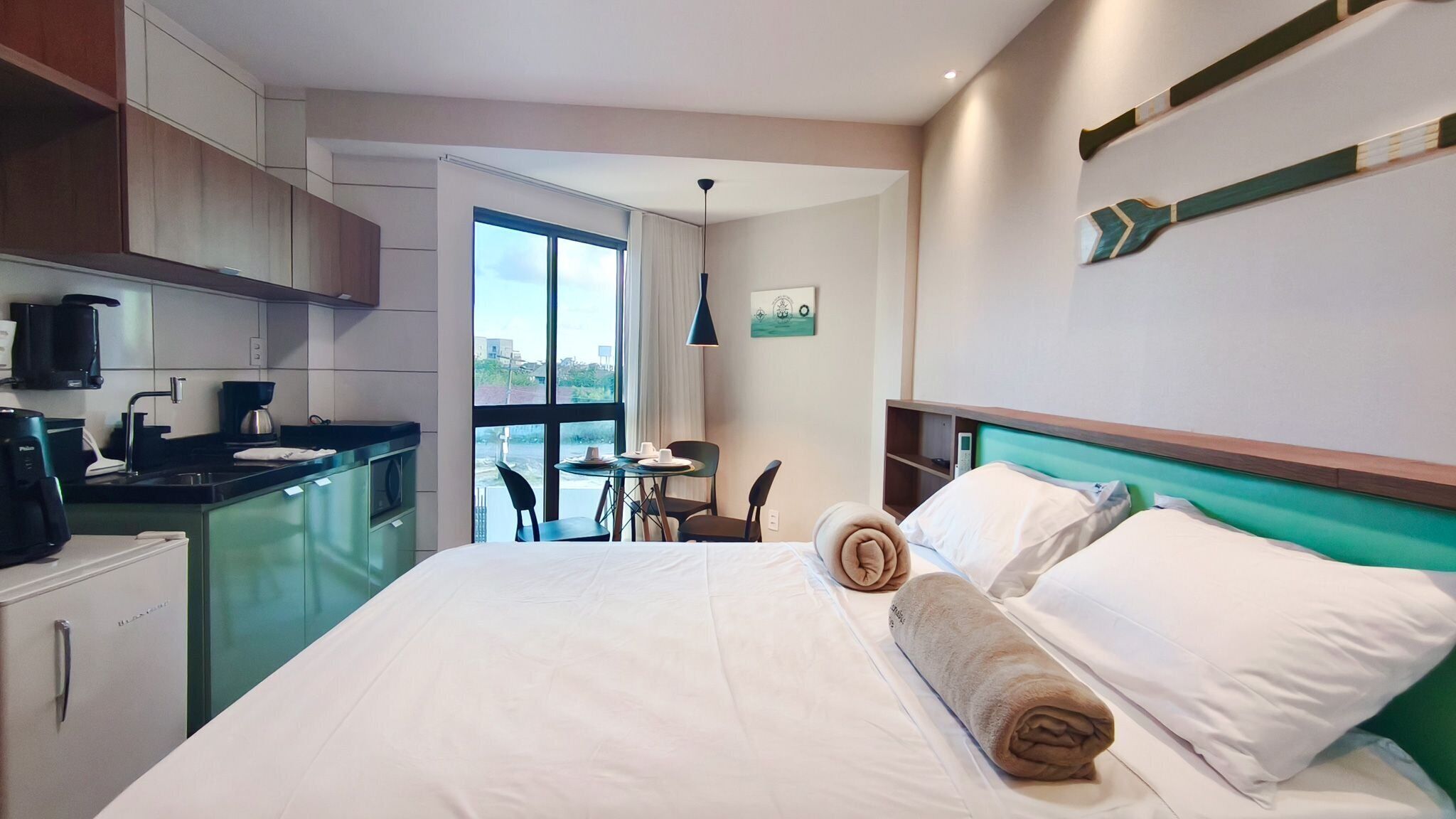 Ein Hotelzimmer mit Bett, einer kleinen Küchenzeile, einem Essbereich und Blick durch ein großes Fenster.