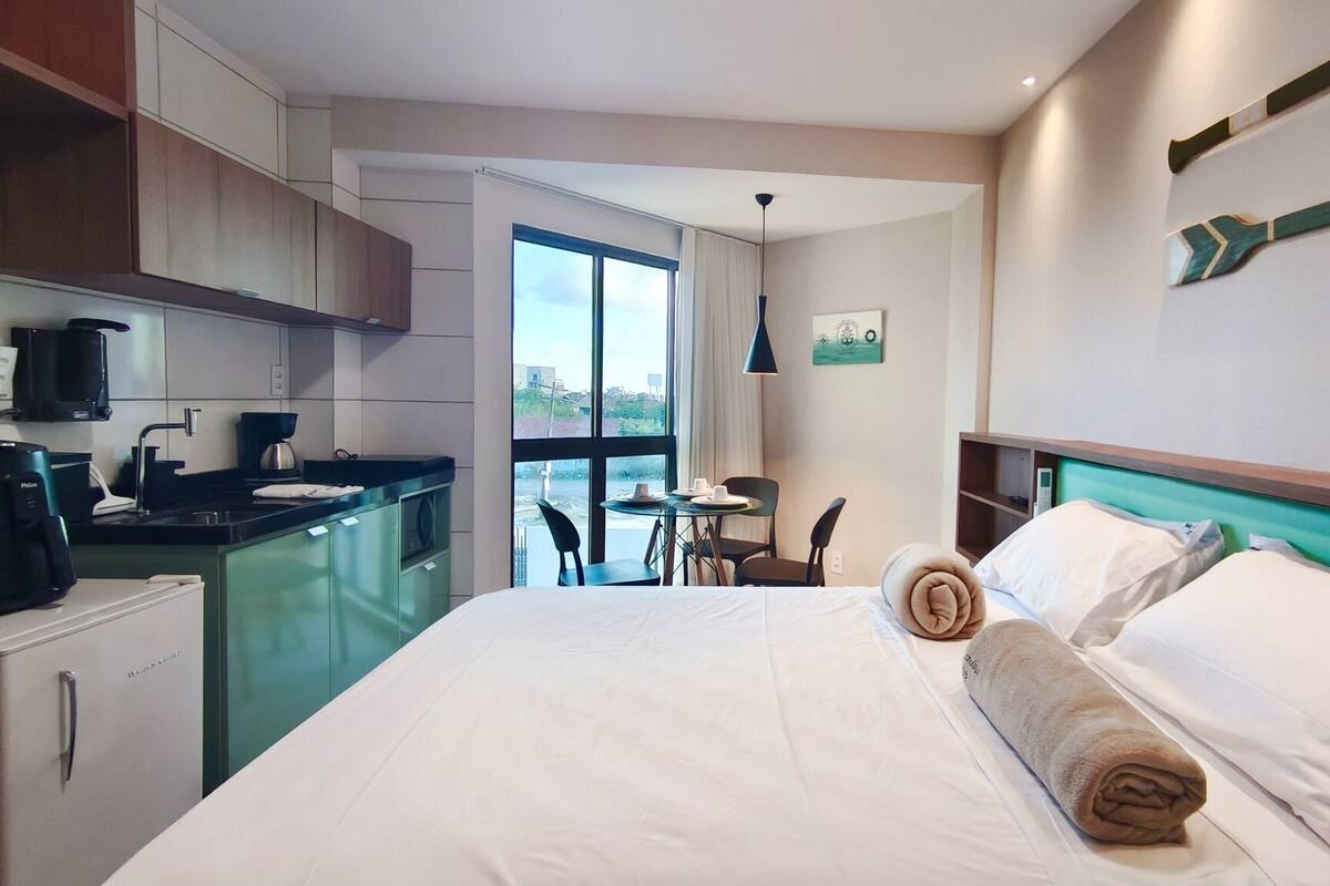 Une chambre d’hôtel comprenant un lit, une petite kitchenette, un coin repas et une vue dégagée sur l’extérieur grâce à une grande fenêtre.