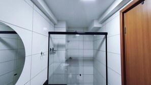 Ein Badezimmer mit weißen Fliesen, einer Duschkabine aus Glas und einer Holztür.