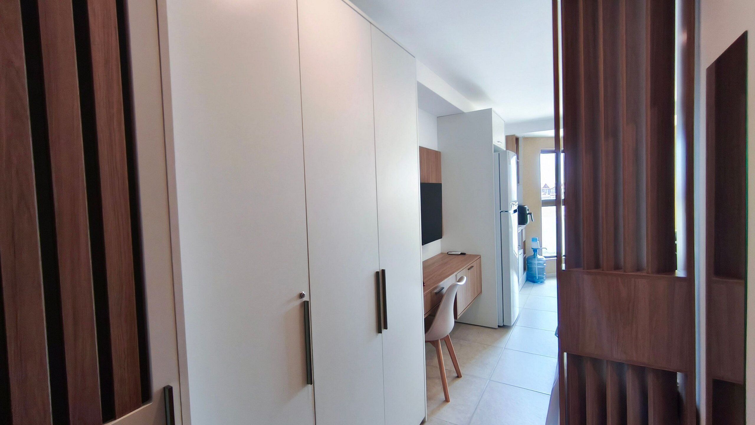 Un couloir avec une armoire blanche, une porte en bois et un coin cuisine comprenant un évier et un plan de travail.