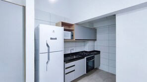 A compact kitchen with a refrigerator, stove, oven, and a microwave on a shelf. - Max Carneiros Suítes  (Tamandaré)