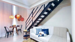 Un salon moderne avec un canapé blanc, une table à manger avec des chaises, un escalier et des œuvres d’art décoratives au mur.