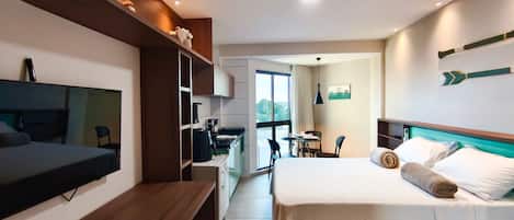 A hotel room with a bed, a desk, a kitchenette, and a TV.