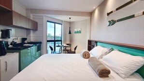 A hotel room with a bed, a small kitchenette, a dining area, and a view through a large window. - Max Carneiros SuÃtes (Tamandaré)