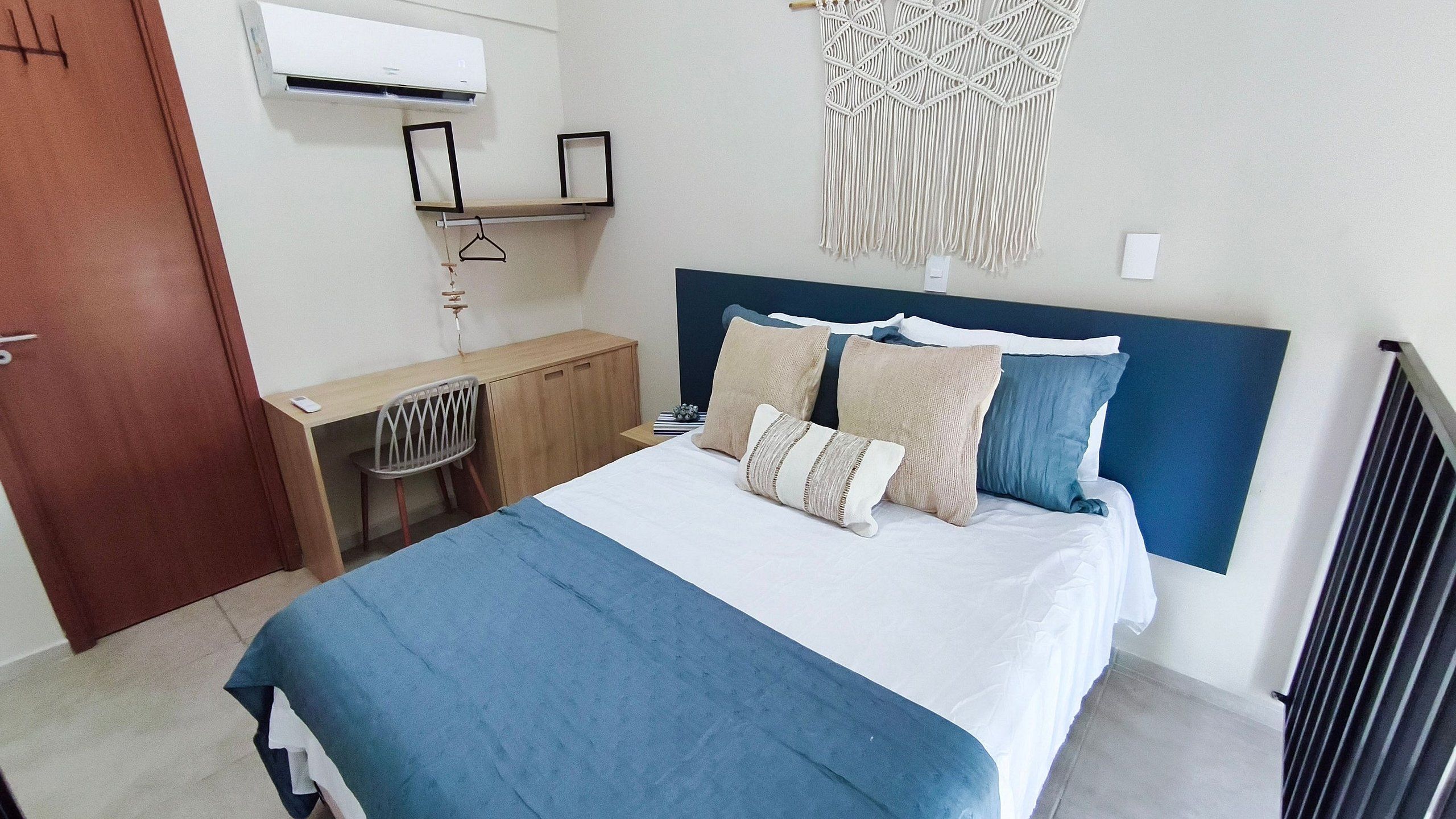Un dormitorio con cama, escritorio, silla, un tapiz de macramé y una puerta.
