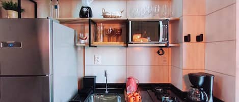 A compact kitchen with a refrigerator, microwave, stove, and a coffee maker.