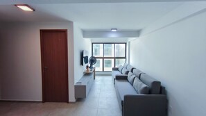 A modern living room with a sofa, a TV, and a fan. - Max Carneiros Suítes  (Tamandaré)