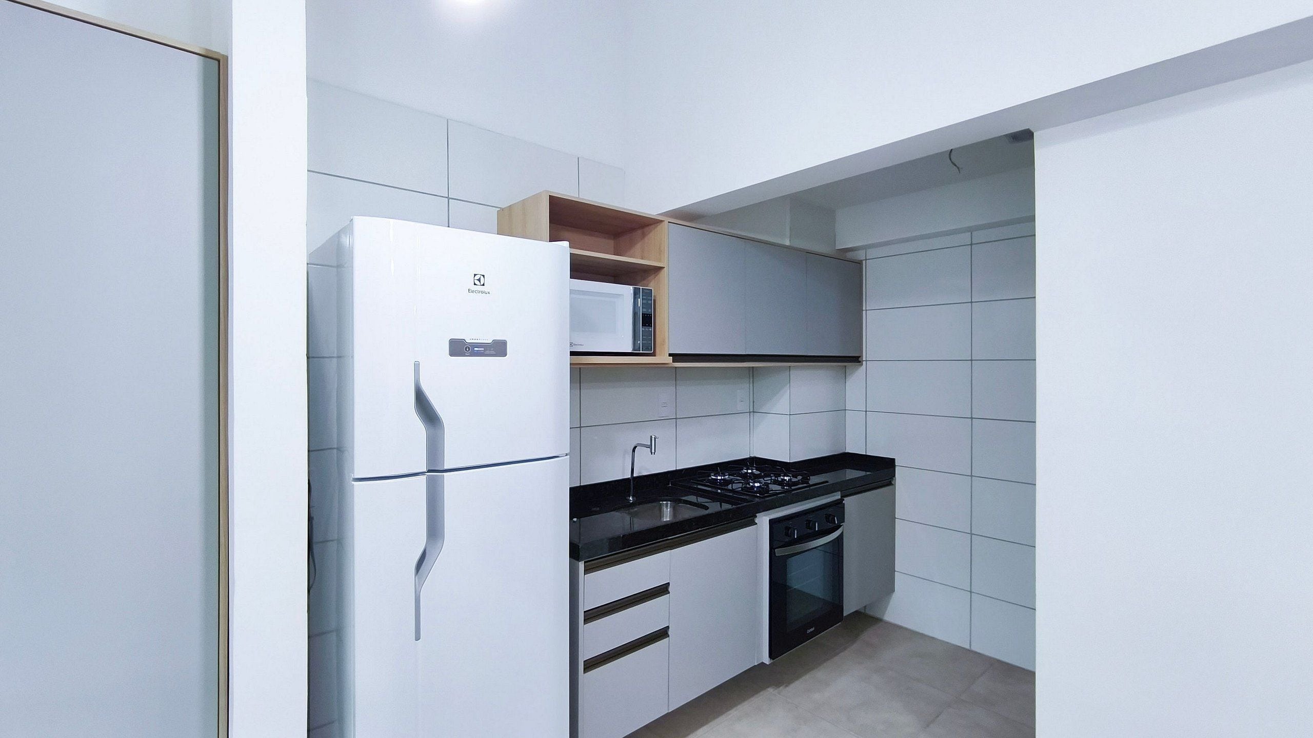 A compact kitchen with a refrigerator, stove, oven, and a microwave on a shelf.