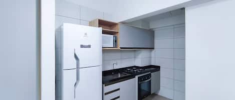 A compact kitchen with a refrigerator, stove, oven, and a microwave on a shelf.