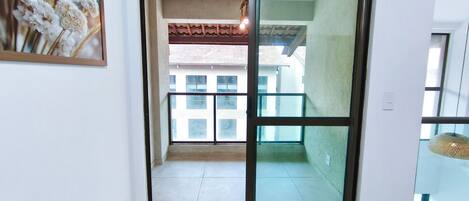 Una habitación con puerta de vidrio corrediza que da a un balcón con vistas a edificios.