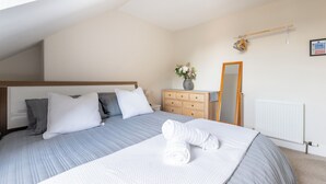 Ein ordentlich bezogenes Bett mit Kissen, ein Schminktisch, ein Spiegel, eine Heizung und ein Fenster mit Blick zum Himmel.