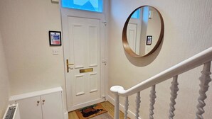 Ein Flur mit einer weißen Tür, einem kleinen Schrank, einem runden Spiegel und einer Treppe mit weißer Handläufung.