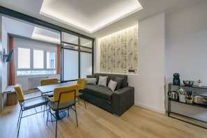A modern living room with a grey sofa, yellow chairs, a dining table, and a kitchen area with utensils. - GRAN VIA capitals, BERLiN (Madrid)