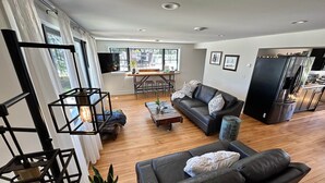 A modern living room with a black leather sofa, wooden coffee table, and a dining area with a table and chairs. - SchoolHouse Pent-House (Elkhart Lake)