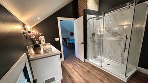 A modern bathroom with a glass shower enclosure, a white vanity with a towel stack, and a wooden floor. - SchoolHouse Pent-House (Elkhart Lake)