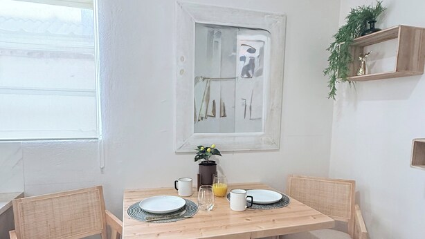A dining area with a wooden table, two chairs, a window, a shelf with a plant, and a wall-mounted picture. - Cozy Hideaway near Mambo Beach - Private Garden (Willemstad)