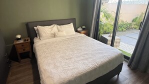 A bedroom with a large bed, wooden flooring, a nightstand, and a view through a glass door to an outdoor area. - Cozy Hideaway near Mambo Beach - Private Garden (Willemstad)