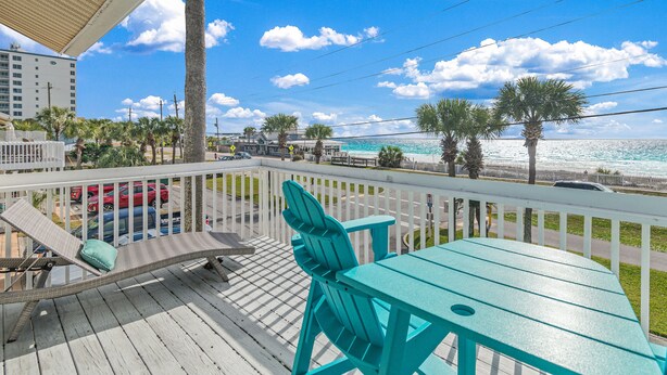 A wooden deck with a table and chairs, overlooking a beach with palm trees and a clear blue sky. - Sand Pebbles 2*Private Beach*Pet Friendly*Big Views*Beach Gear (Destin)