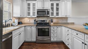 A modern kitchen with white cabinetry, stainless steel appliances, and a granite countertop. - Sand Pebbles 2*Private Beach*Pet Friendly*Big Views*Beach Gear (Destin)