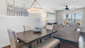 A dining area with a wooden table, cushioned chairs, and a hanging light fixture. - Sand Pebbles 2*Private Beach*Pet Friendly*Big Views*Beach Gear (Destin)