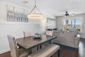 A dining area with a wooden table, cushioned chairs, and a hanging light fixture. - Sand Pebbles 2*Private Beach*Pet Friendly*Big Views*Beach Gear (Destin)