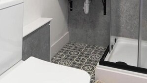 Un baño con inodoro y lavamanos blancos, cerramiento de ducha de vidrio y baldosas de suelo con diseño.