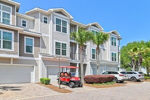 Un edificio residencial de varios pisos con un garaje, un carrito de golf rojo y dos coches aparcados.