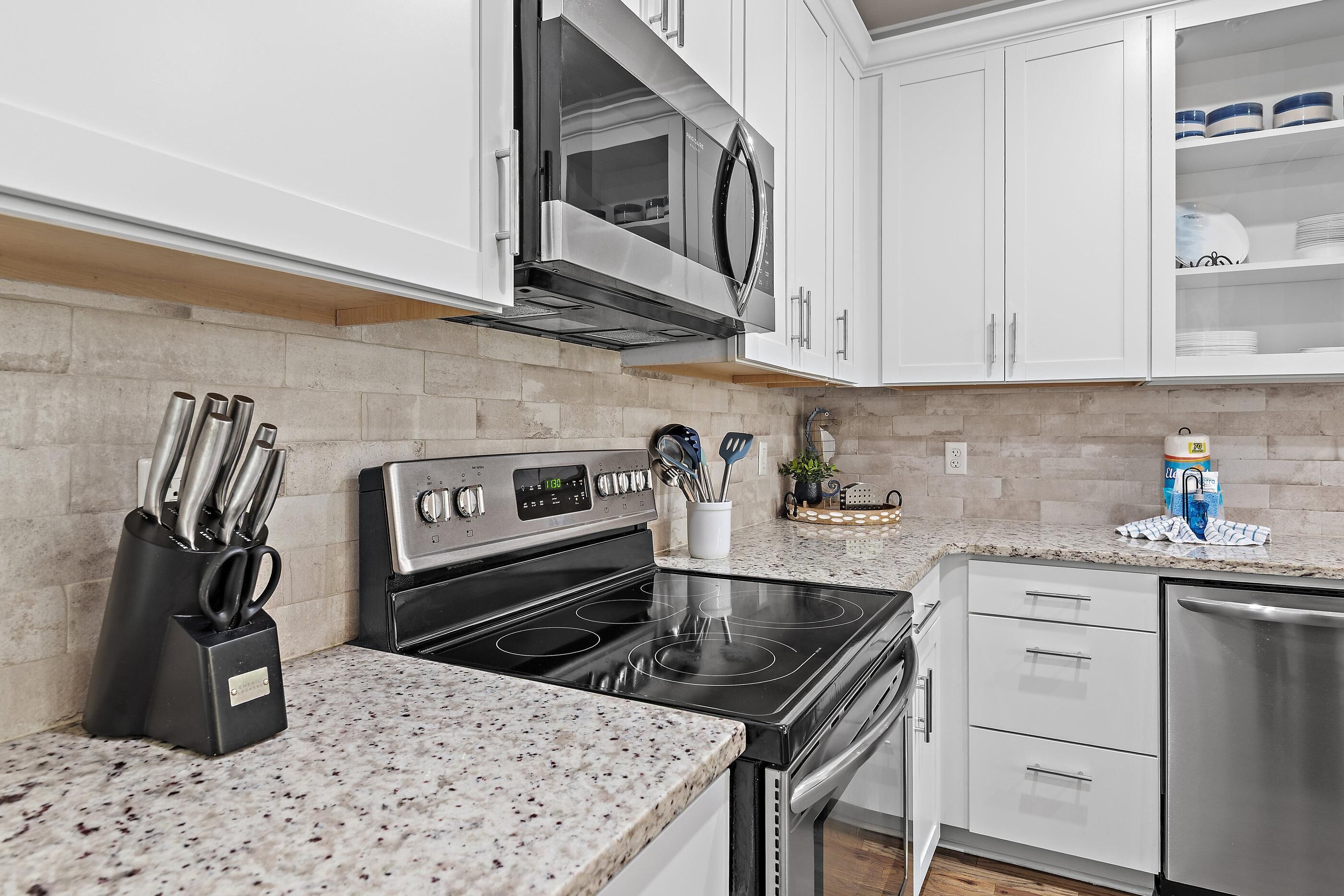 A kitchen with white cabinets, a stainless steel microwave, a black stove, and a dishwasher.