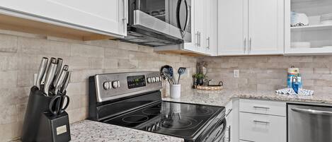 A kitchen with white cabinets, a stainless steel microwave, a black stove, and a dishwasher.