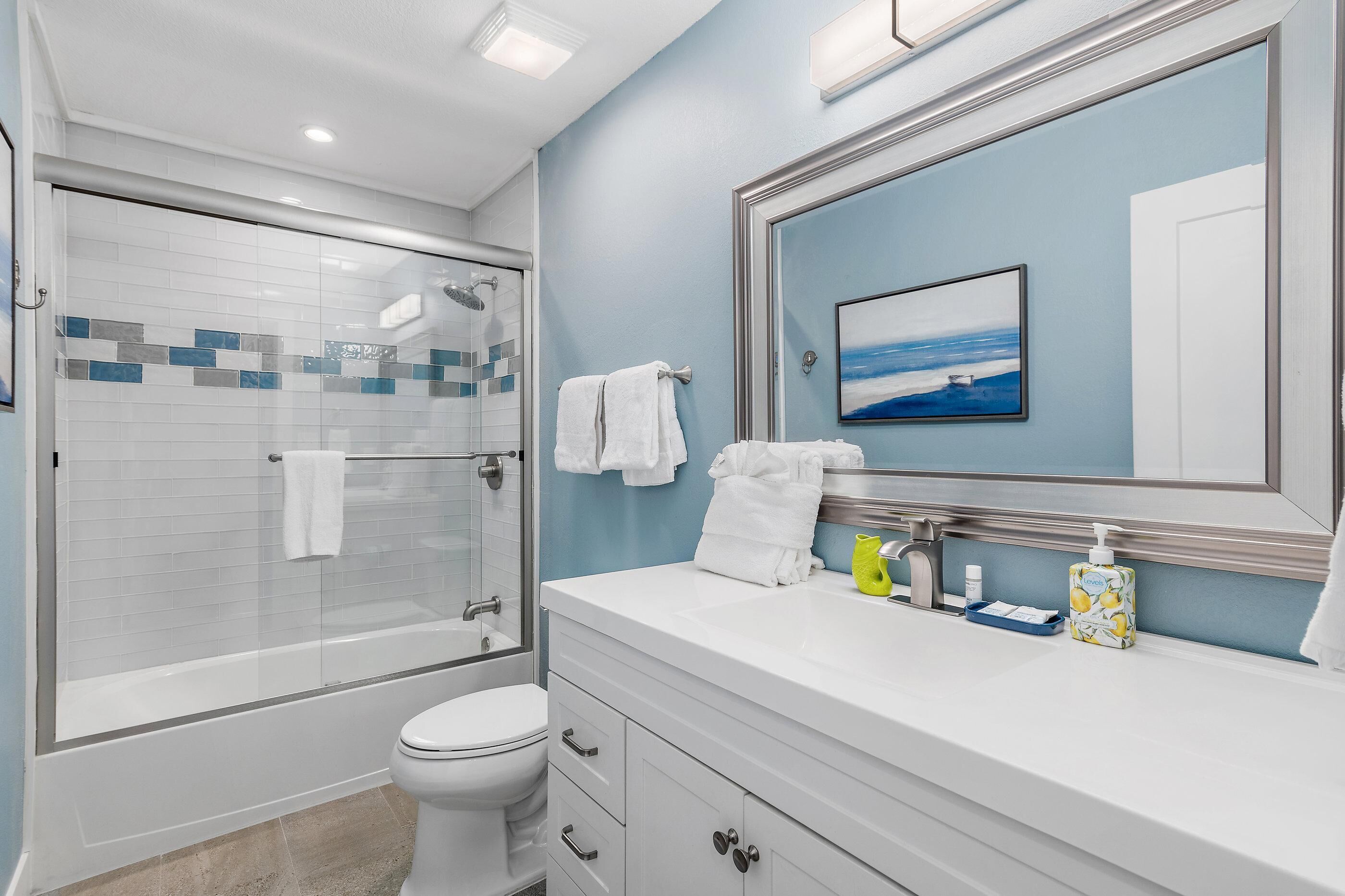 Un baño moderno con ducha envuelta en vidrio, un inodoro blanco y un tocador con un espejo grande.