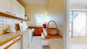 Eine kleine Küche mit weißen Schränken, einer gefliesten Spritzschutzleiste, einer Holzausziehtafel, einer Kaffeemaschine, einem Toaster, einem roten Wasserkocher, einem Korb und einem Fenster mit Blick.
