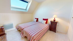 Une chambre à coucher avec un lit, une table de chevet, une lampe, un radiateur et une fenêtre.