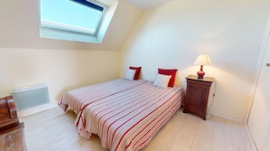 Ein Schlafzimmer mit einem Bett, einem Nachttisch, einer Lampe, einem Heizkörper und einem Fenster.