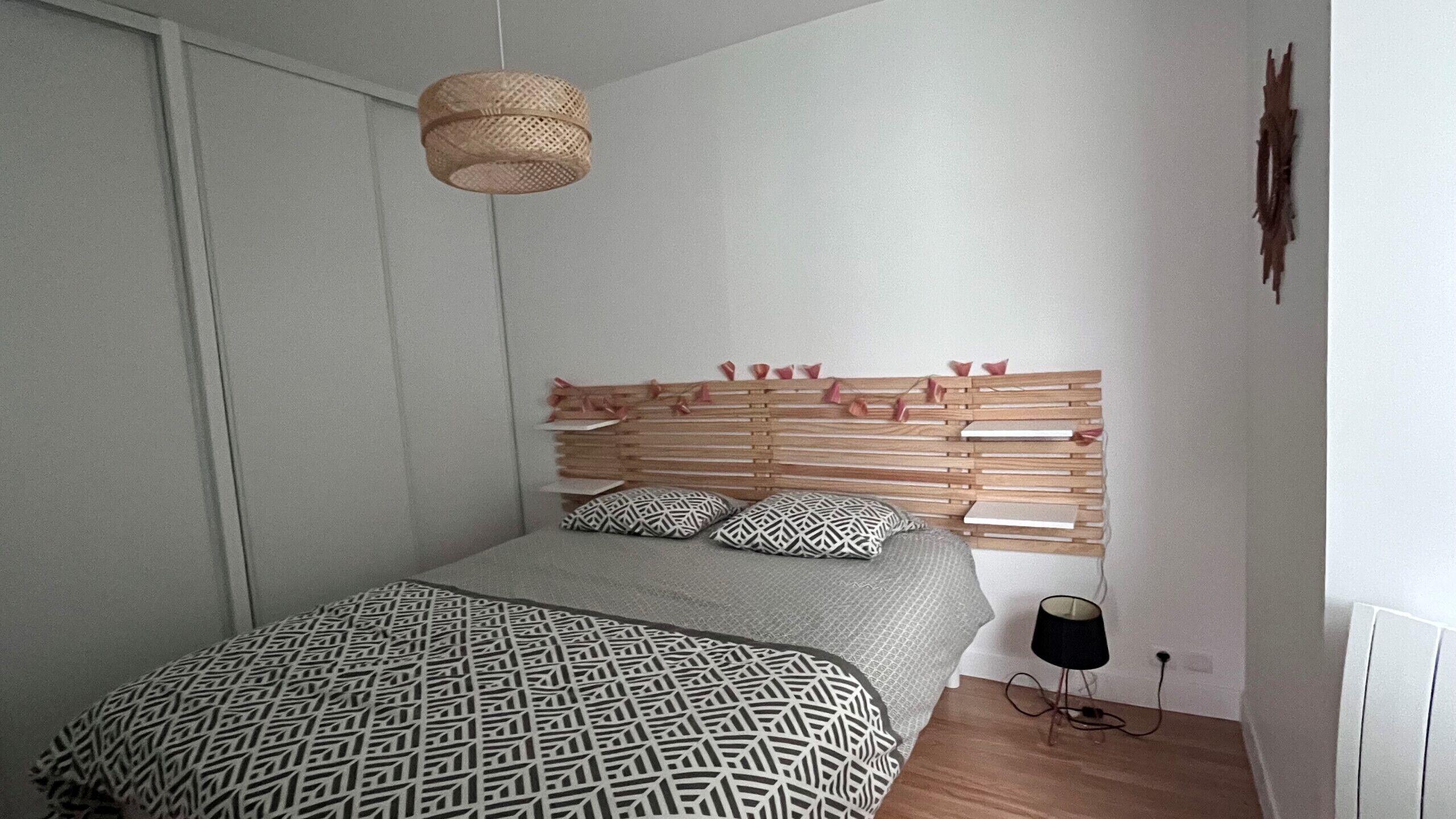 Een slaapkamer met een bed, nachtkastje, lamp en een wandplank.