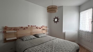A bedroom with a bed, a bedside table, a hanging light fixture, a wall-mounted mirror, and a window with curtains. - Le Cocon de la Paludiere (Le Pouliguen)