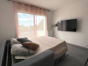 Una camera da letto moderna con un letto, una TV a parete e un'ampia finestra con tende.