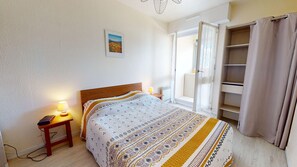 A bedroom with a bed, bedside lamps, a nightstand, a window with curtains, and a door. - Pavois d'Azur - Sea view apartment 100m from the beach (Saint-Hilaire-de-Riez)