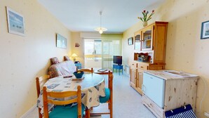 A compact living space with a dining table, chairs, a sofa, a TV, and a kitchenette. - Pavois d'Azur - Sea view apartment 100m from the beach (Saint-Hilaire-de-Riez)