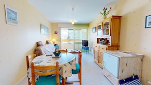 A compact living space with a dining table, chairs, a sofa, a TV, and a kitchenette. - Pavois d'Azur - Sea view apartment 100m from the beach (Saint-Hilaire-de-Riez)