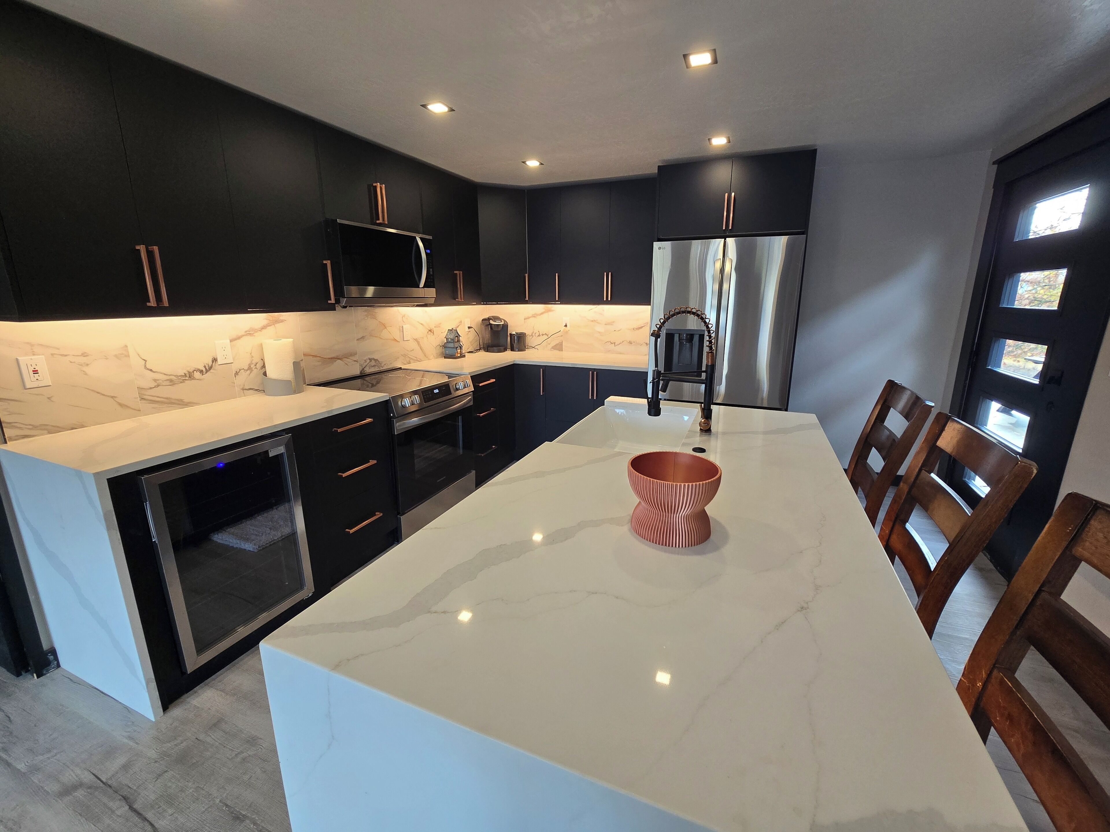 Una cocina moderna con armarios oscuros, encimera de mármol blanco y electrodomésticos de acero inoxidable.
