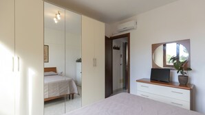 Un dormitorio con una cama, un armario, un tocador, un televisor y una planta en maceta.