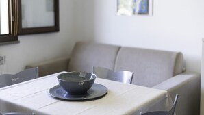 Una mesa de comedor con un bol sobre un posavasos, una silla y un sofá en una habitación con un espejo y un cuadro en la pared.